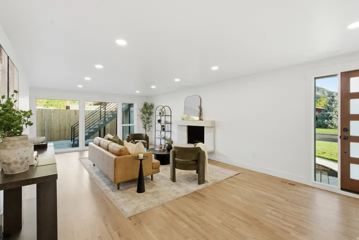 Recessed lighting, wood-finish flooring, white walls, stone fireplace, and a multi-paneled wood entry door
