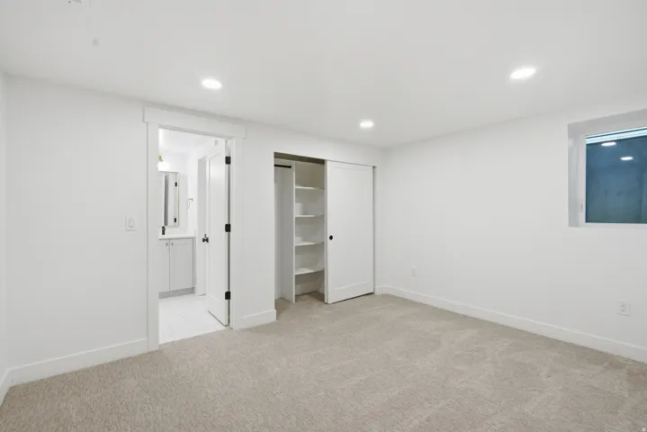 Recessed lighting, light-colored carpeting, a built-in closet with shelving, and a window with a white frame
