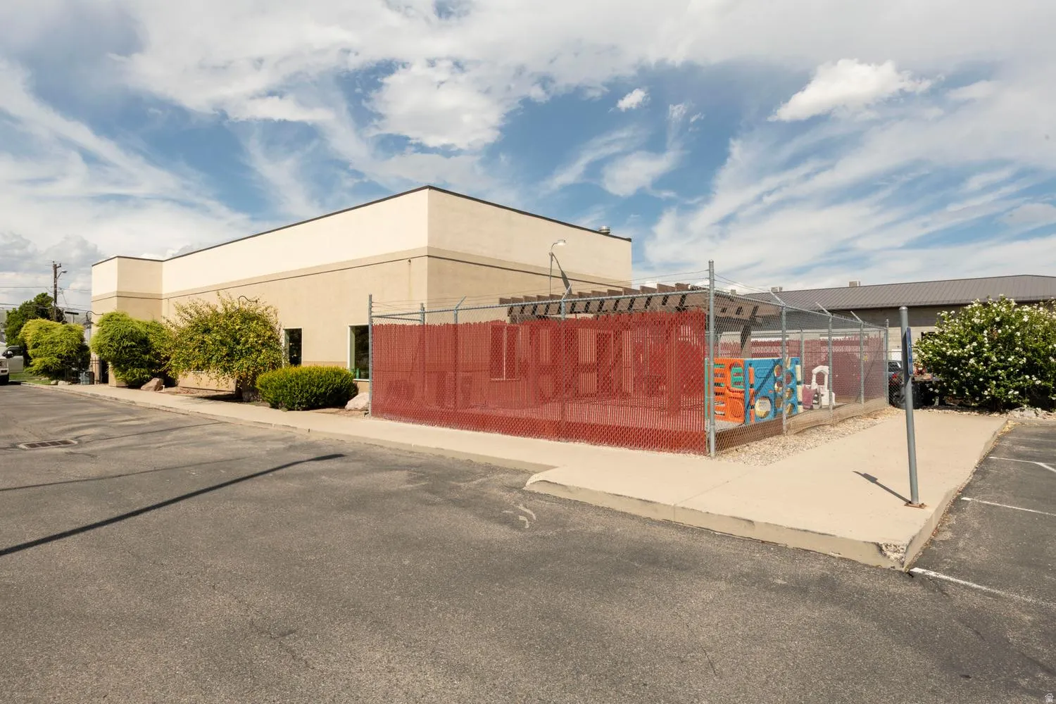 Exterior building with light-toned stucco and dark trim, featuring a fenced utility area with a red mesh screen