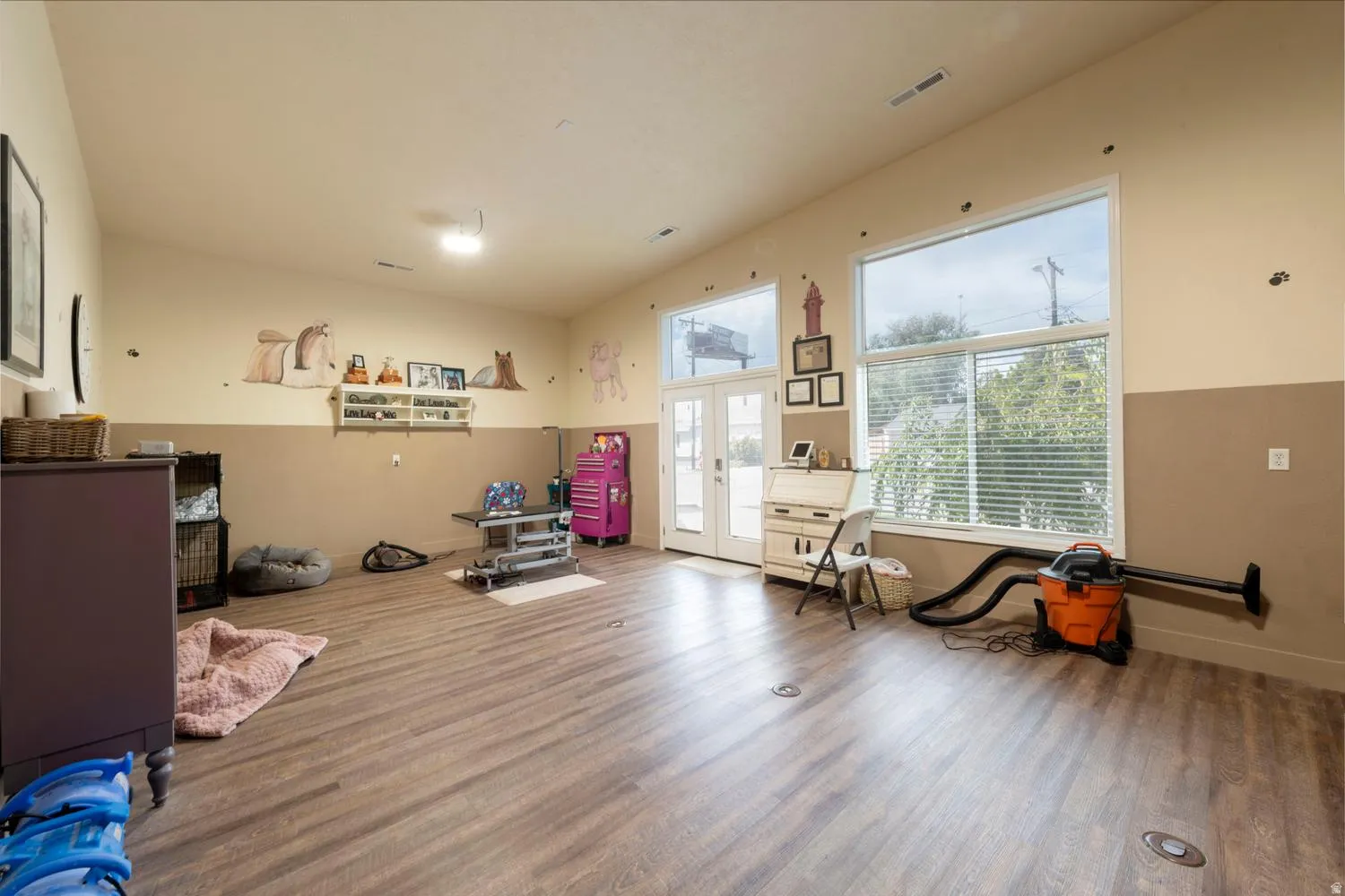Spacious room featuring wood-finish flooring, high ceilings, large windows with blinds, and French doors