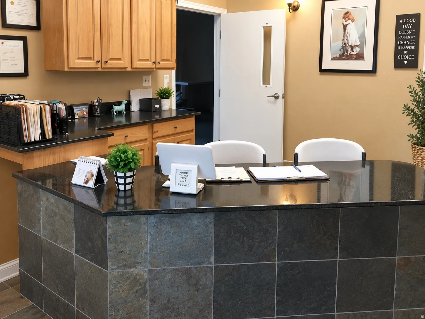 Tiled reception desk with a polished dark countertop, light wood-finish cabinetry, and neutral wall paint