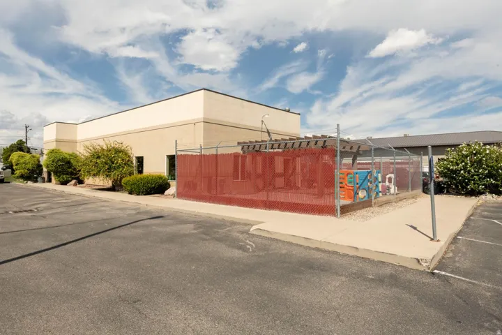 Exterior building with light-toned stucco and dark trim, featuring a fenced utility area with a red mesh screen