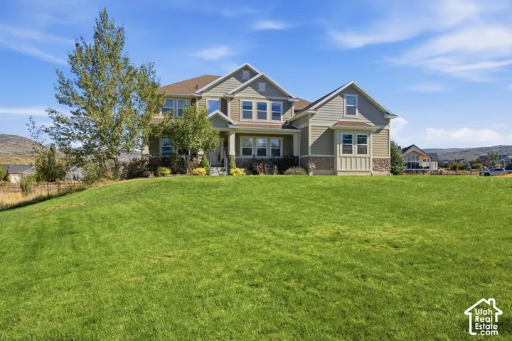 Expansive green lawn with mature trees and a multi-level residence featuring gabled roofs, stone accents, and multiple windows