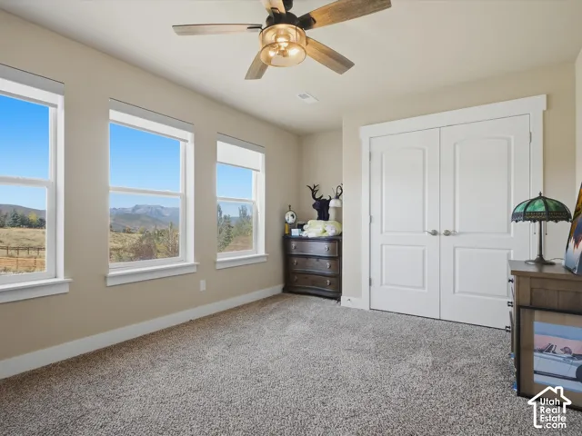 Three large windows, textured carpeting, a ceiling fan with integrated lighting, and double bi-fold doors