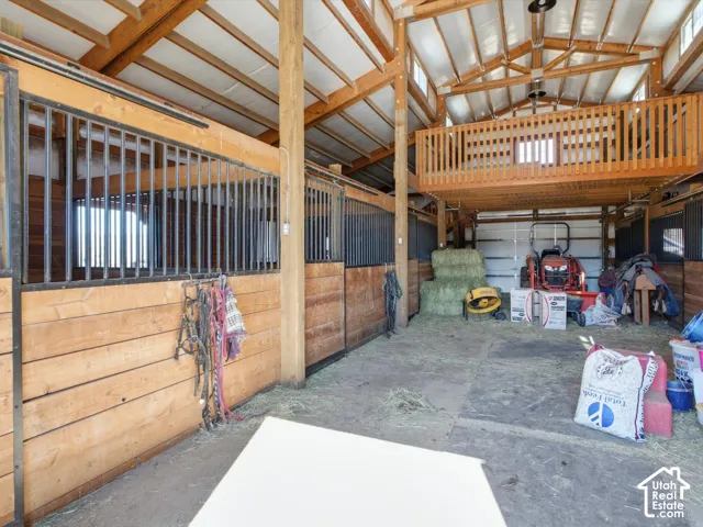 Barn interior featuring exposed wood beams, multiple stalls with metal grates, a hay loft with wood railings, and a concrete floor
