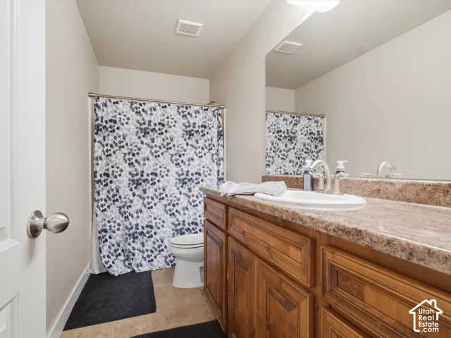 Bathroom featuring a wood-finish vanity with a built-in sink, a large wall-mounted mirror, and tile flooring