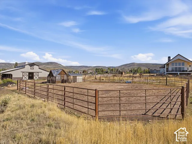 Fenced outdoor arena, large barn with white trim, additional outbuildings, expansive property with distant hills