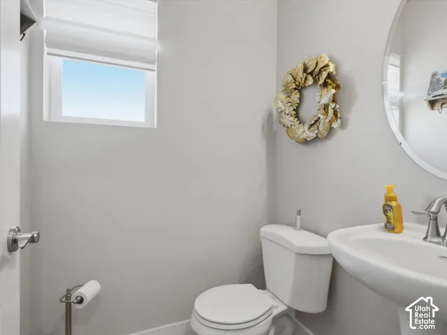 Pedestal sink, wall-mounted mirror, and a window with a roman shade