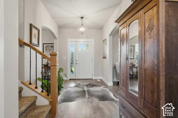 Arched entryway leading to a solid white front door with sidelight, wood-finish flooring, and a decorative chandelier