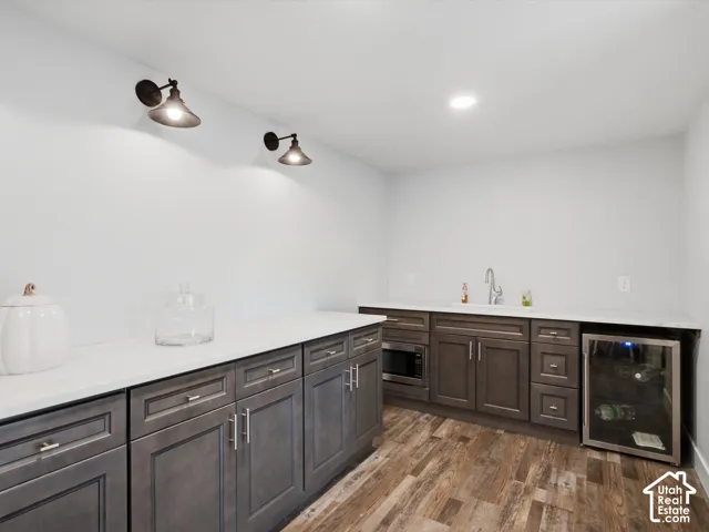 Extensive cabinetry with white countertops, wood-finish flooring, built-in microwave, and beverage refrigerator