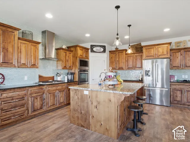Kitchen featuring wood cabinetry, stainless steel appliances, a center island with a granite-style countertop, a tile backsplash, and pendant lighting