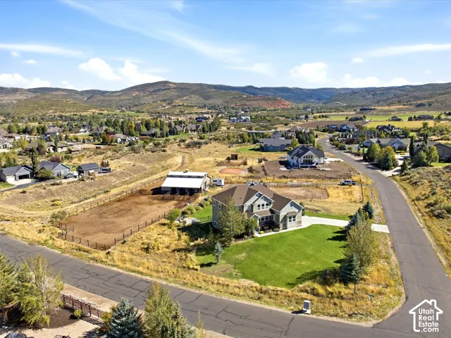 Spacious residential lot featuring a large single-family home with a two-car garage, expansive green lawn, and a fenced equestrian arena with an accompanying barn