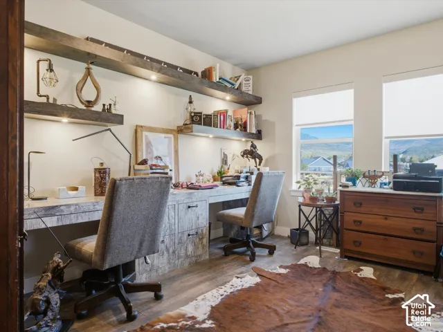 Wood-finish flooring, built-in desk with rustic wood finish, integrated shelving with accent lighting, multiple windows with roller shades, and a wood-finish chest of drawers