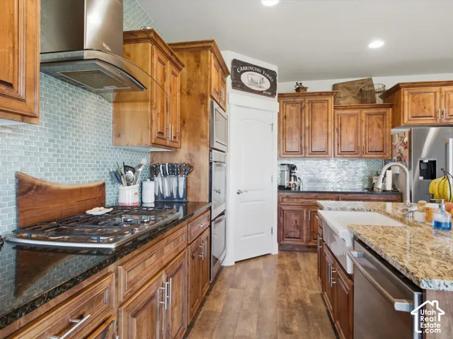 Wood-finish flooring, wood cabinetry, built-in double oven, gas range, and a farmhouse sink with a polished faucet