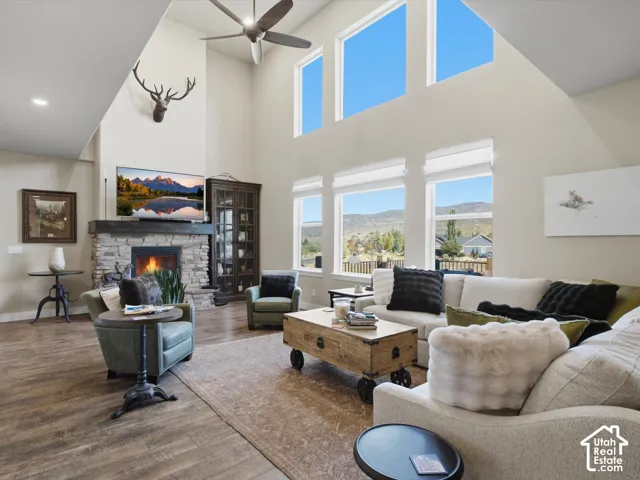 Vaulted ceiling with a ceiling fan, stone-clad fireplace with a wood mantle, wood-finish flooring, and multiple windows