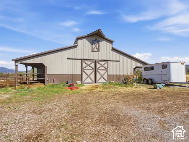 Two-tone barn structure featuring a gabled roof, sliding barn doors, an attached covered lean-to, and an exterior light fixture
