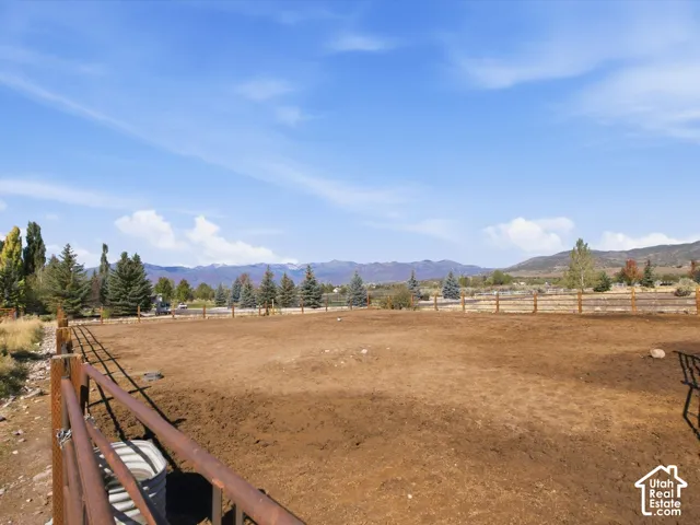 Expansive outdoor area featuring a metal fence, wood rail fencing, established trees, and distant mountain scenery