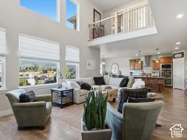 Vaulted ceilings, expansive windows, wood-finish flooring, an open-concept kitchen, and an upper-level balcony with wrought iron railing