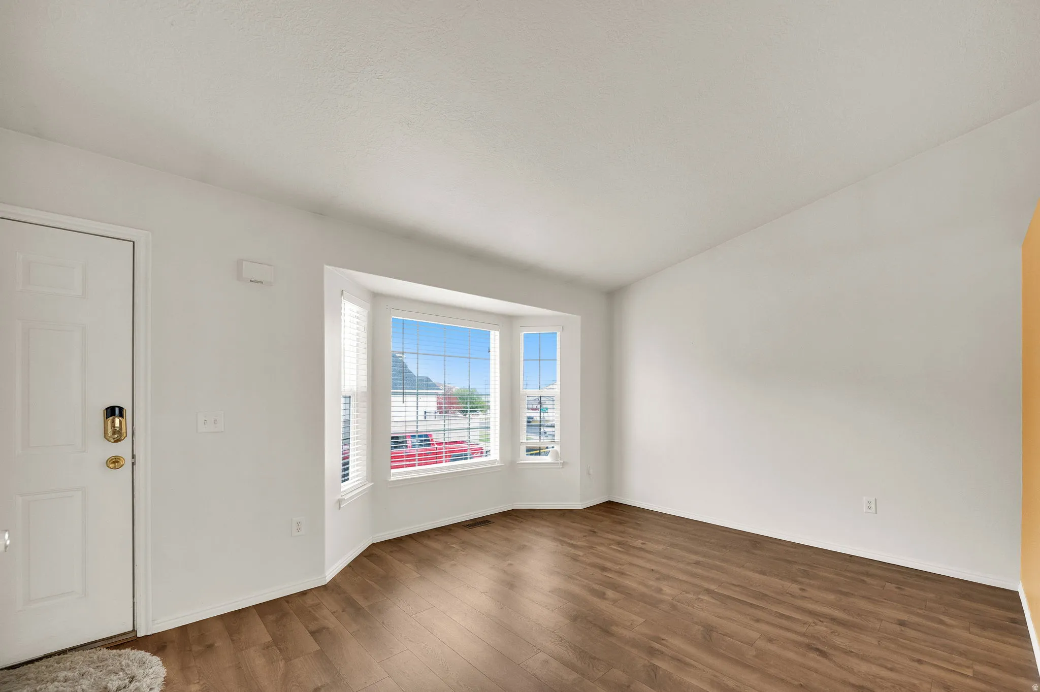 Bay window with horizontal blinds, wood-finish flooring, white paneled door, and bright white walls