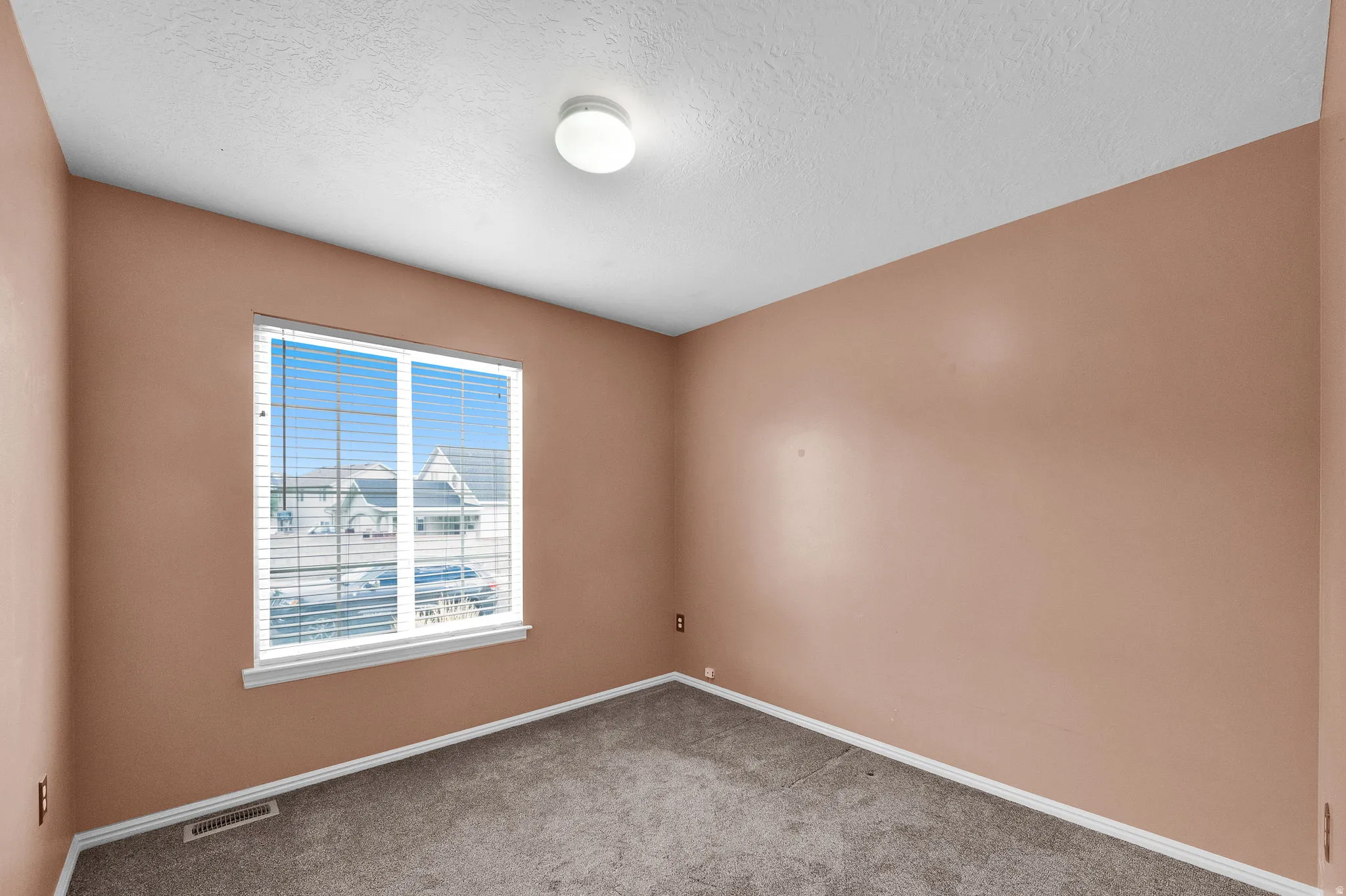 Recessed window with white trim, tan wall paint, textured ceiling, and gray carpet flooring