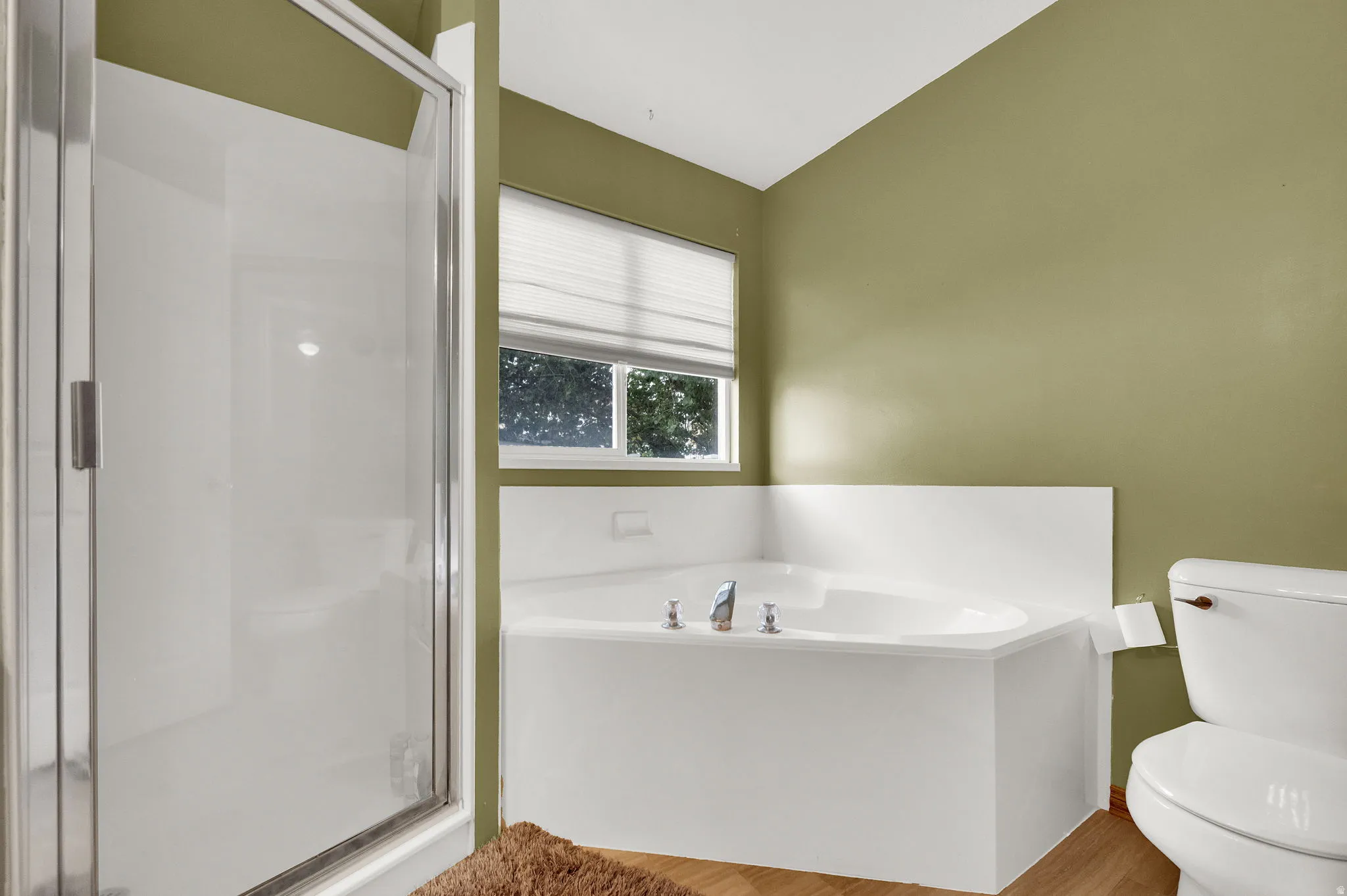MASTER BATHROOM. White corner soaking tub with deck-mounted fixtures, wood-finish flooring, and a glass-enclosed shower