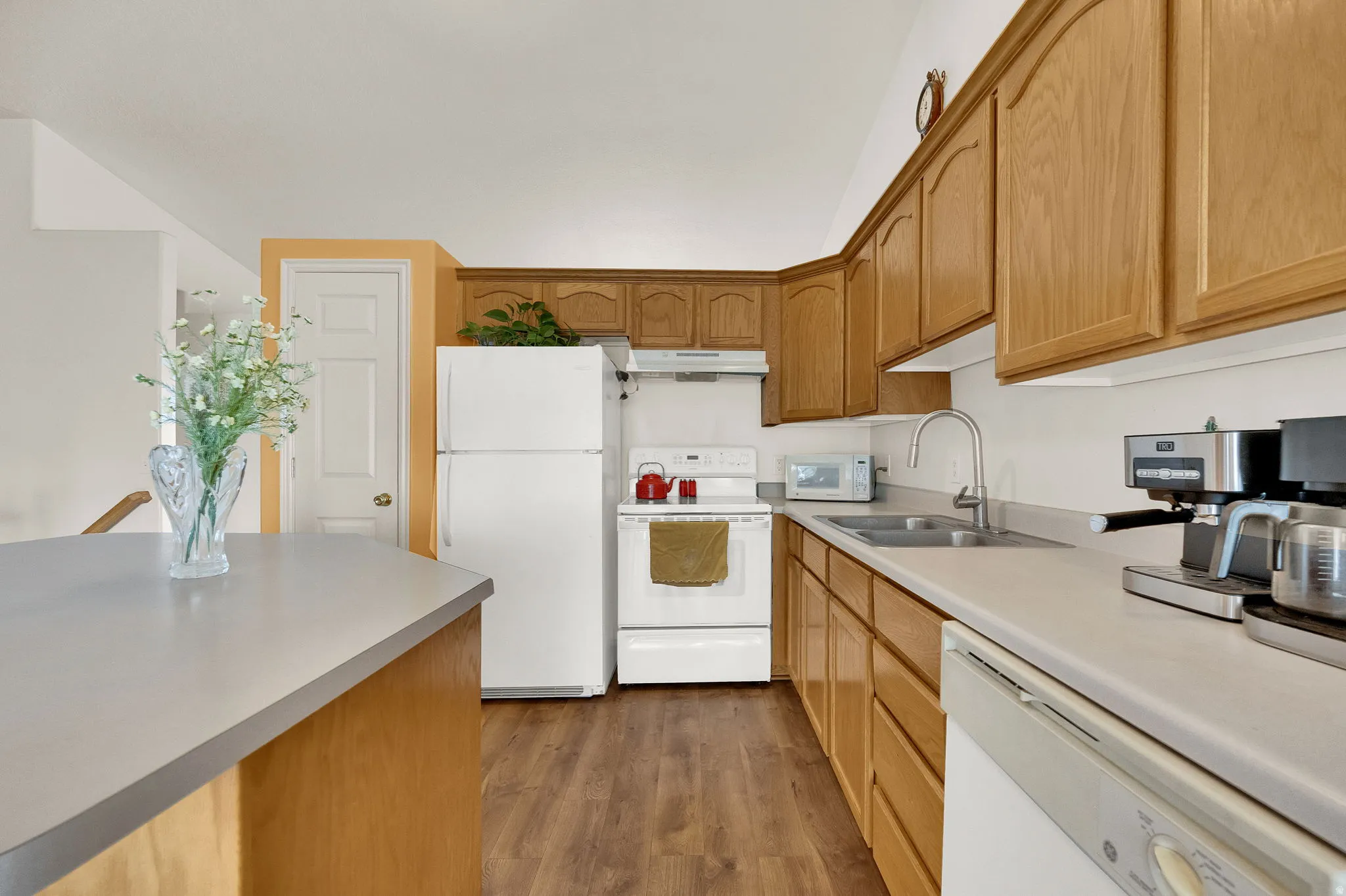 Kitchen with wood-finish flooring, light wood cabinetry, white appliances, and a double basin sink