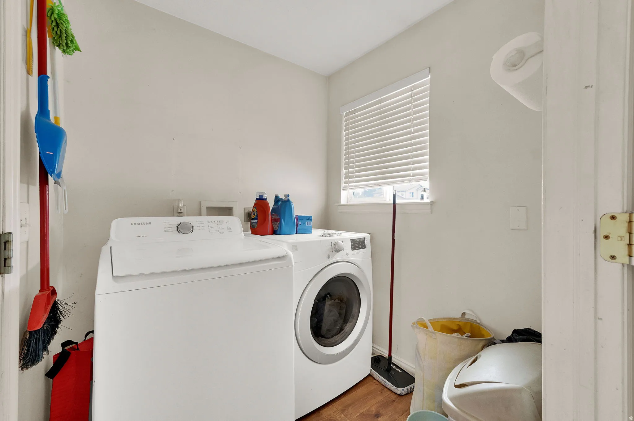 Laundry area featuring wood-finish flooring and a window with blinds