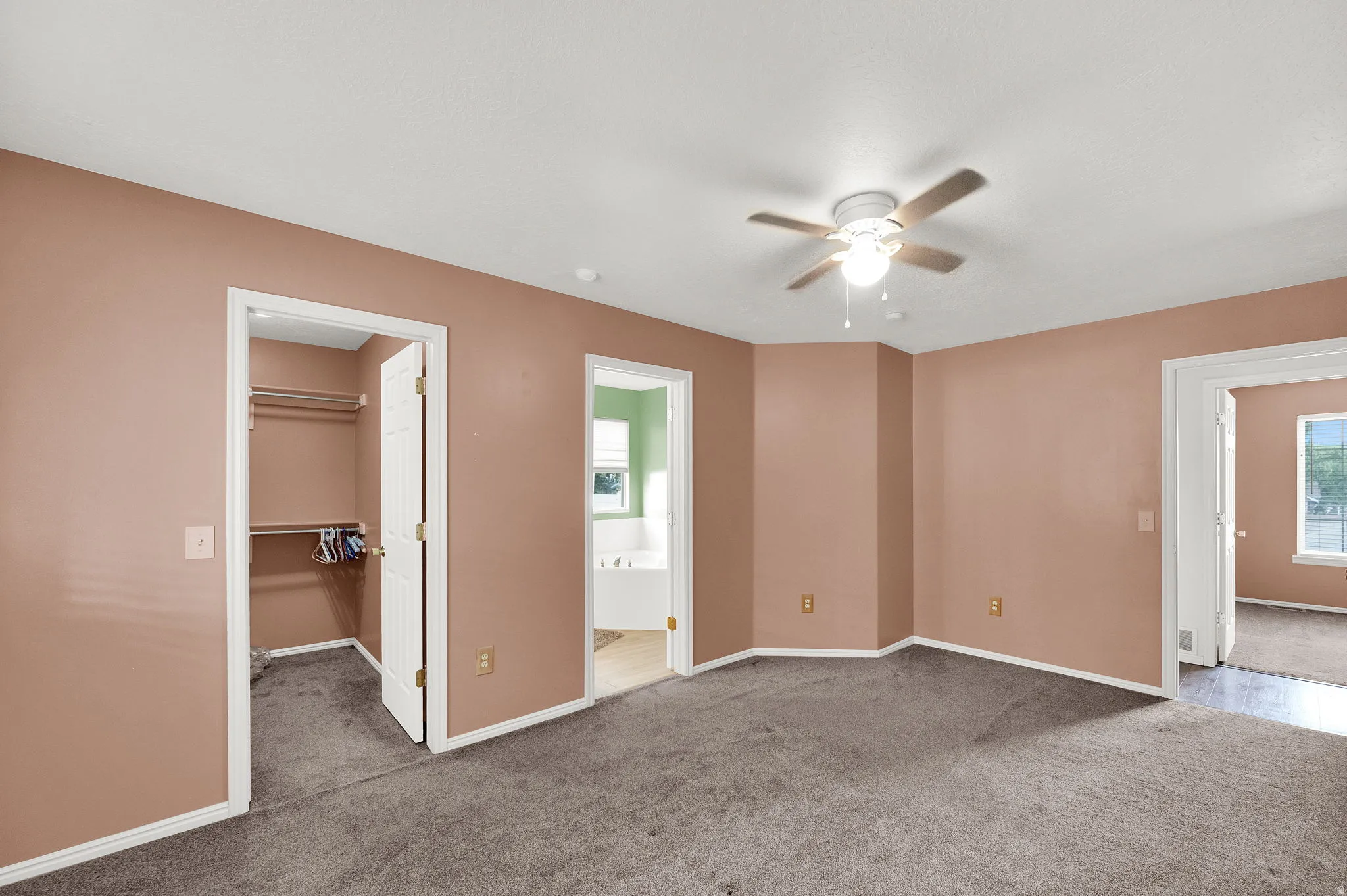 Neutral-toned walls, plush carpeting, ceiling fan with integrated lighting, and a walk-in closet with built-in shelving