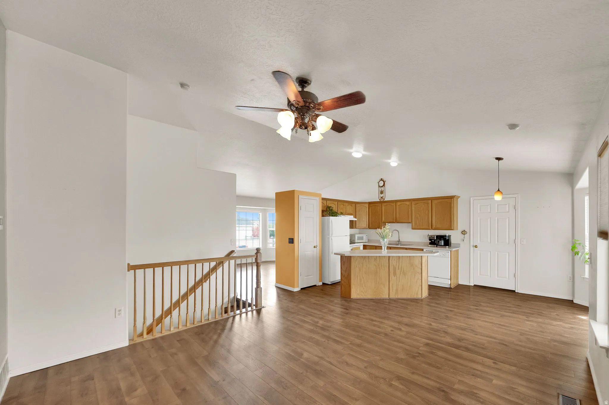 Open-concept living space featuring wood-finish flooring, vaulted ceilings, and a kitchen with light wood cabinetry