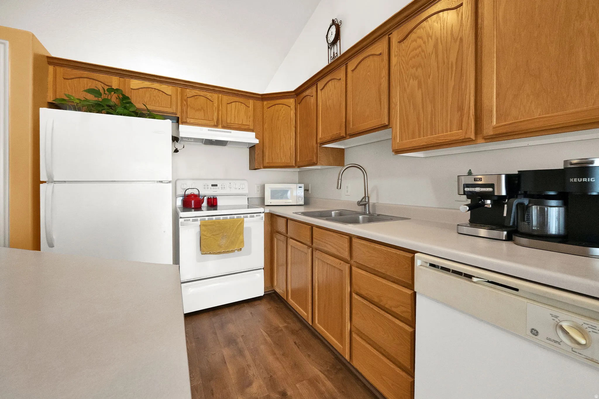 Kitchen featuring wood-finish cabinetry, white appliances, laminate countertops, a stainless steel sink, and wood-finish flooring