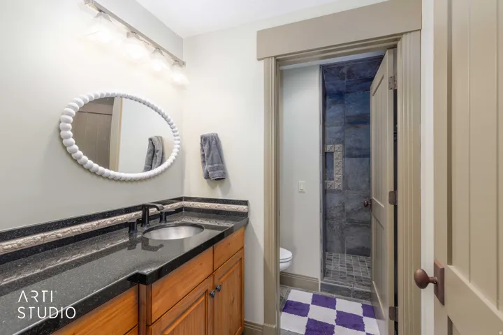 Wood-finish vanity with a dark countertop and undermount sink.  Walk-in shower view.