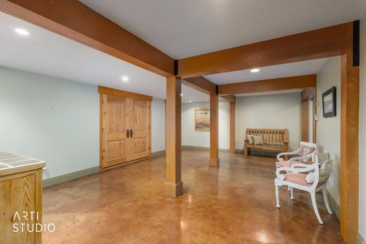 Exposed wood beams and columns, light-colored walls, wood-finish double doors, recessed lighting, and stained cement flooring