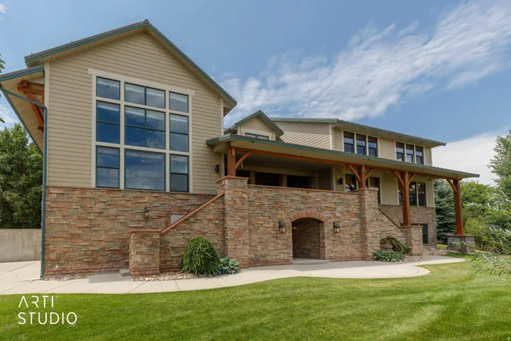 Stone facade with an arched entry, large picture windows, and a covered patio with exposed wood beams