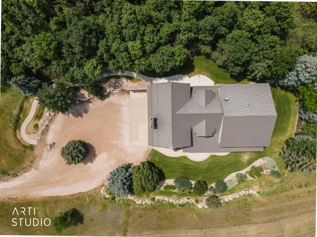 Gable roofline, expansive gravel driveway, curved concrete pathways, mature perimeter trees, and landscaped shrubbery