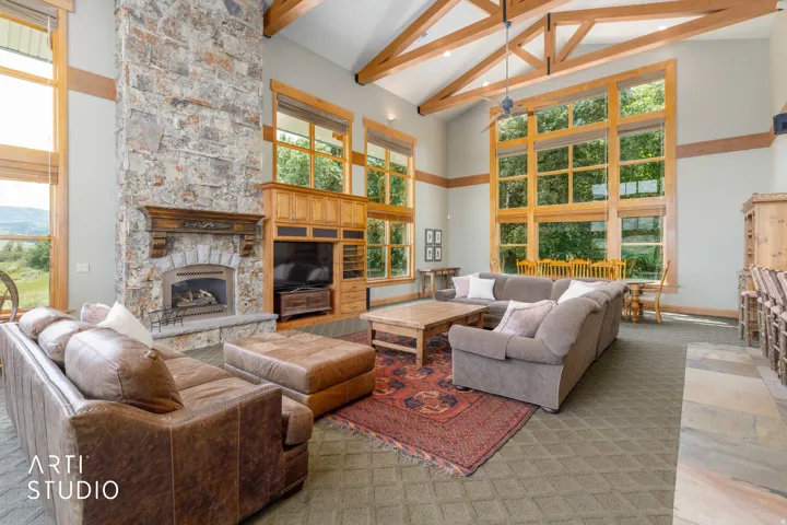 Large and spacious great room! Vaulted ceilings with exposed wood beams, rock  fireplace, built-in cabinetry, expansive wood-clad windows with custom wood casing,
