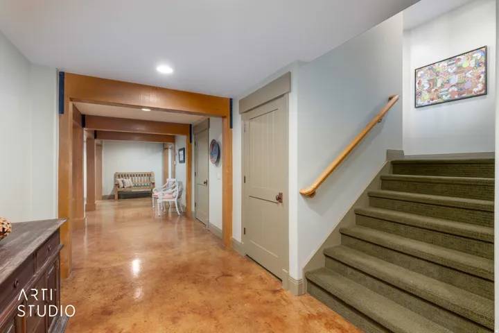 Exposed wood beam accents throughout, stained concrete flooring, carpeted staircase with wood handrail