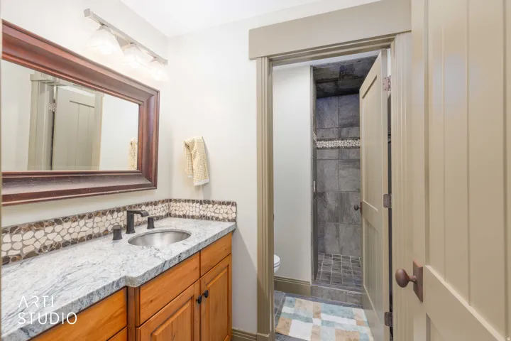 Full bath with walk-in shower, wood-finish vanity with a silver-toned vessel sink, custom tile accents.