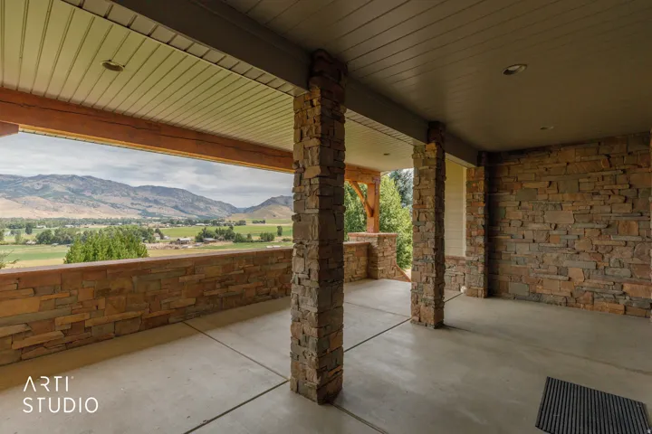 Covered front patio featuring stone-clad pillars, stone-clad perimeter wall, concrete flooring.