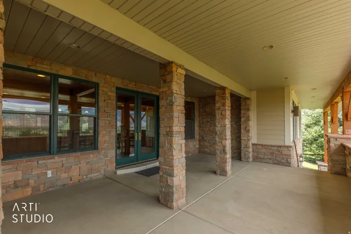 View from front porch to the kitchen. Spacious covered patio with stone-faced columns, concrete flooring, and recessed lighting