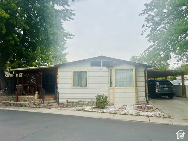 Siding exterior, covered entry porch with lattice detailing, bay window, covered carport, and mature trees