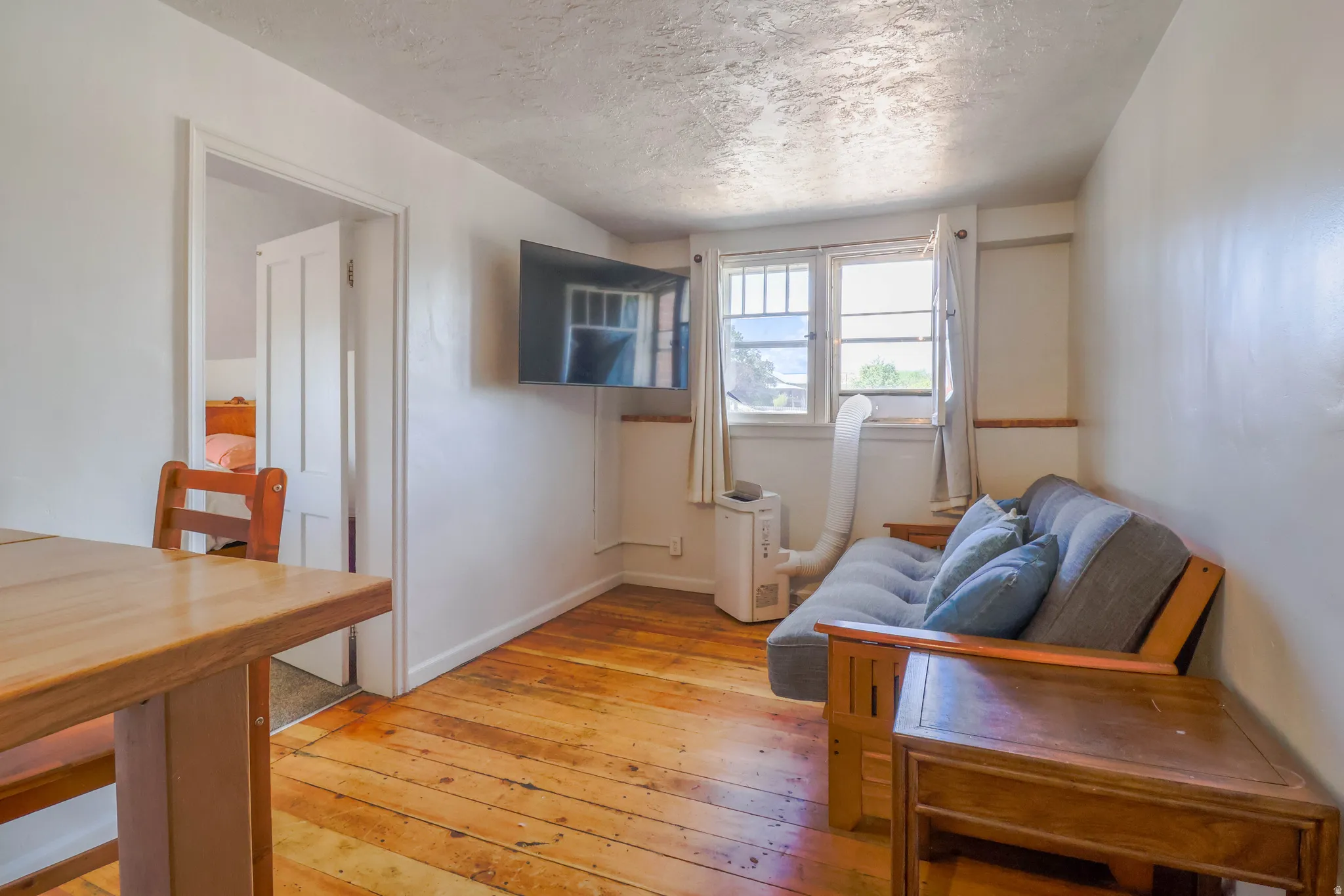 Hardwood flooring, white painted walls, window with natural light, textured ceiling