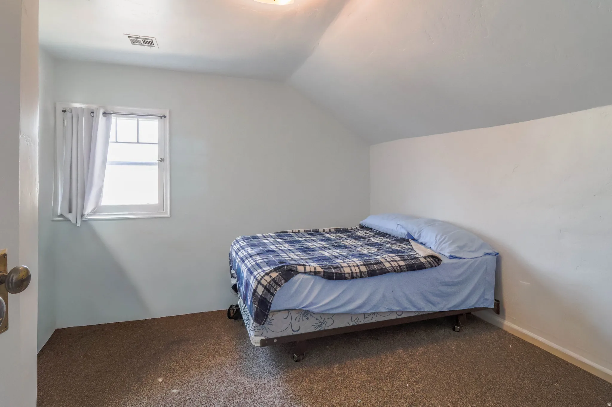 Sloped ceiling room featuring a single window and textured carpeting