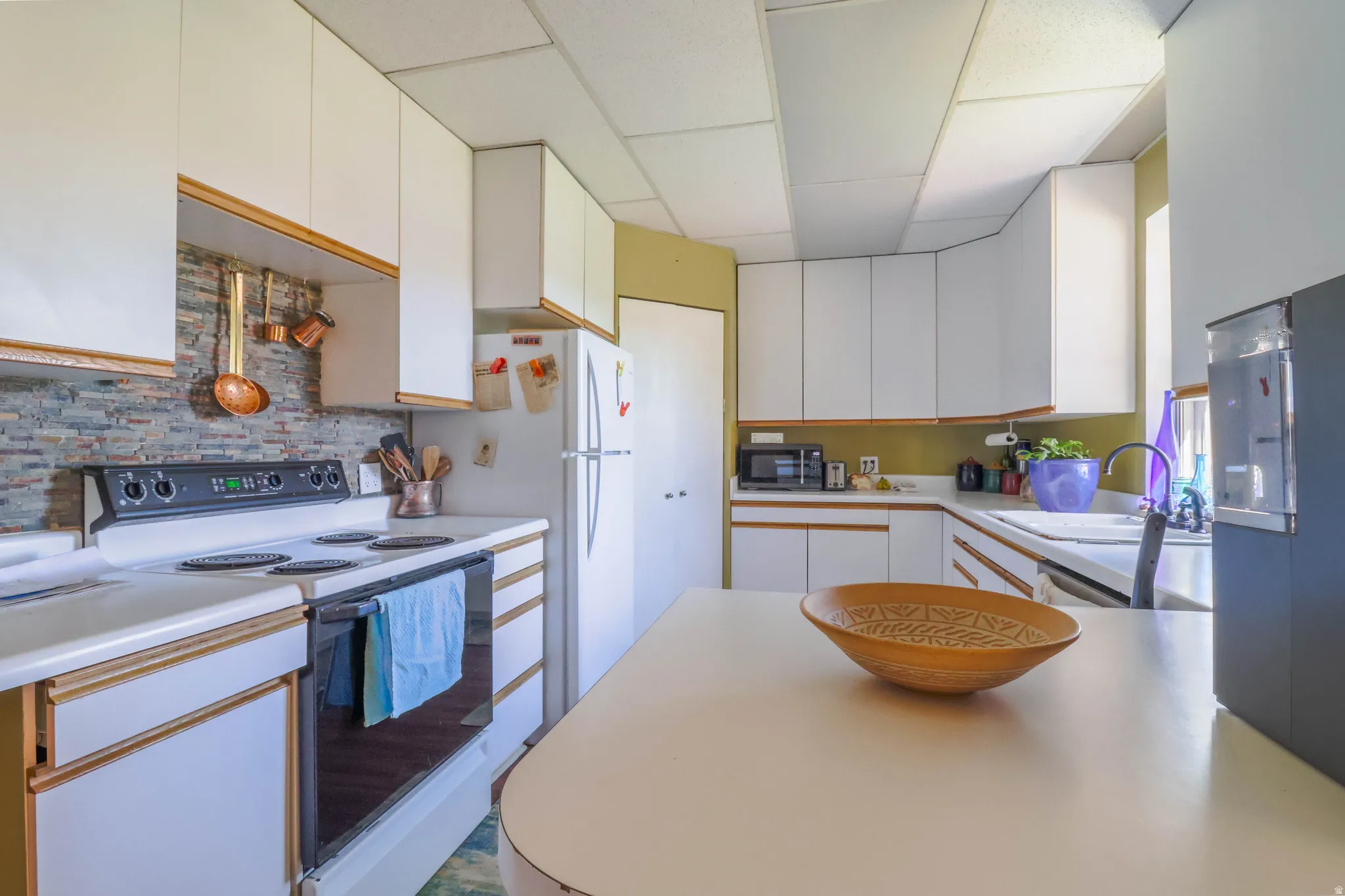 White cabinetry with wood-finish trim, a stone-finish backsplash, and an integrated white oven range
