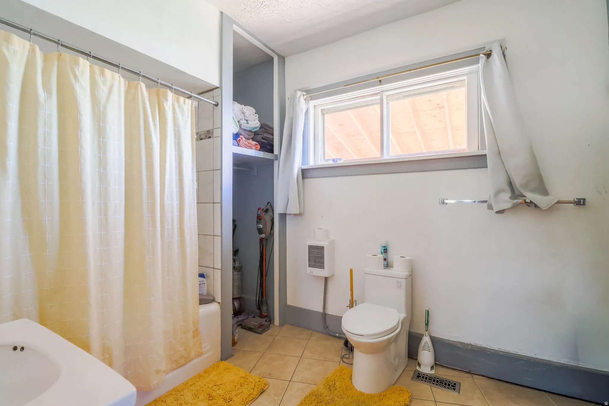 Built-in shelving, tiled shower surround, window with trim, wall-mounted towel bar, and tile flooring