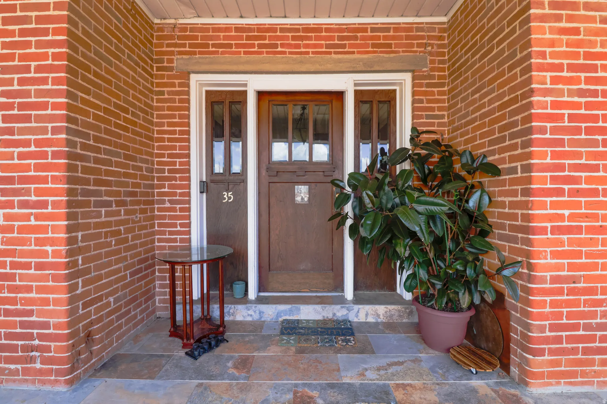 Brick exterior with a wood entry door, glass sidelights, and slate tile flooring