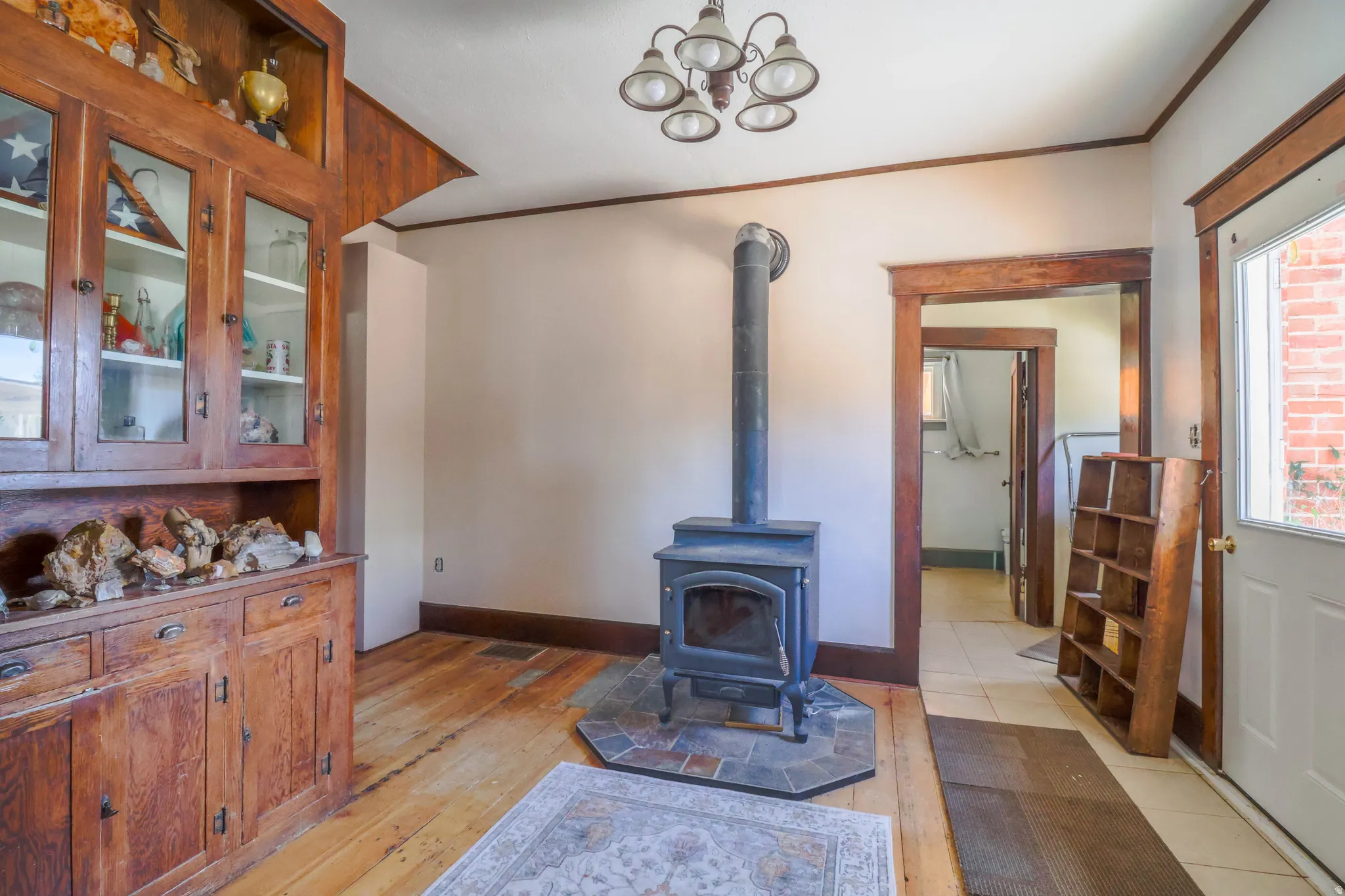 Hardwood flooring, built-in wooden hutch with glass-front cabinetry, a wood-burning stove with a tiled hearth, and a chandelier lighting fixture