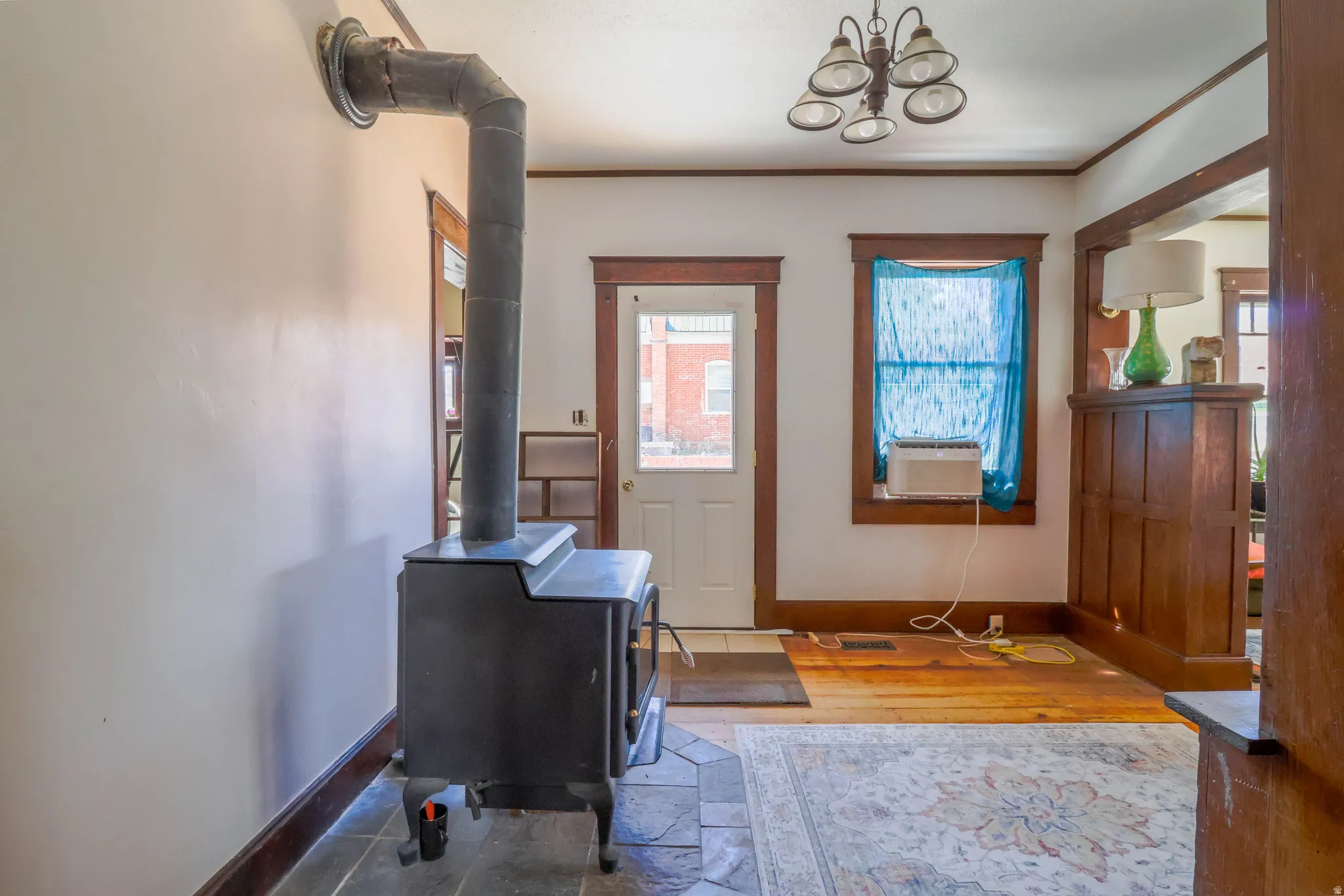 Wood-burning stove with stone tile surround, wood-finish flooring, and a multi-light ceiling fixture