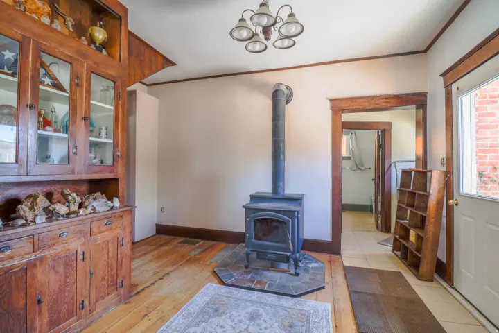 Hardwood flooring, built-in wooden hutch with glass-front cabinetry, a wood-burning stove with a tiled hearth, and a chandelier lighting fixture