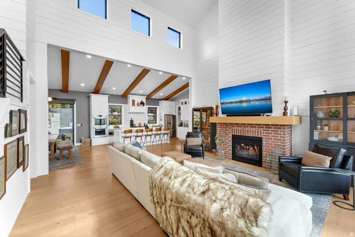 Vaulted ceilings with clerestory windows, wood-finish flooring, a brick fireplace with a wood mantel, and exposed ceiling beams