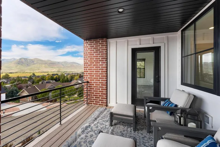 Covered exterior balcony featuring a wood-finish floor, black metal railing, and brick accent wall